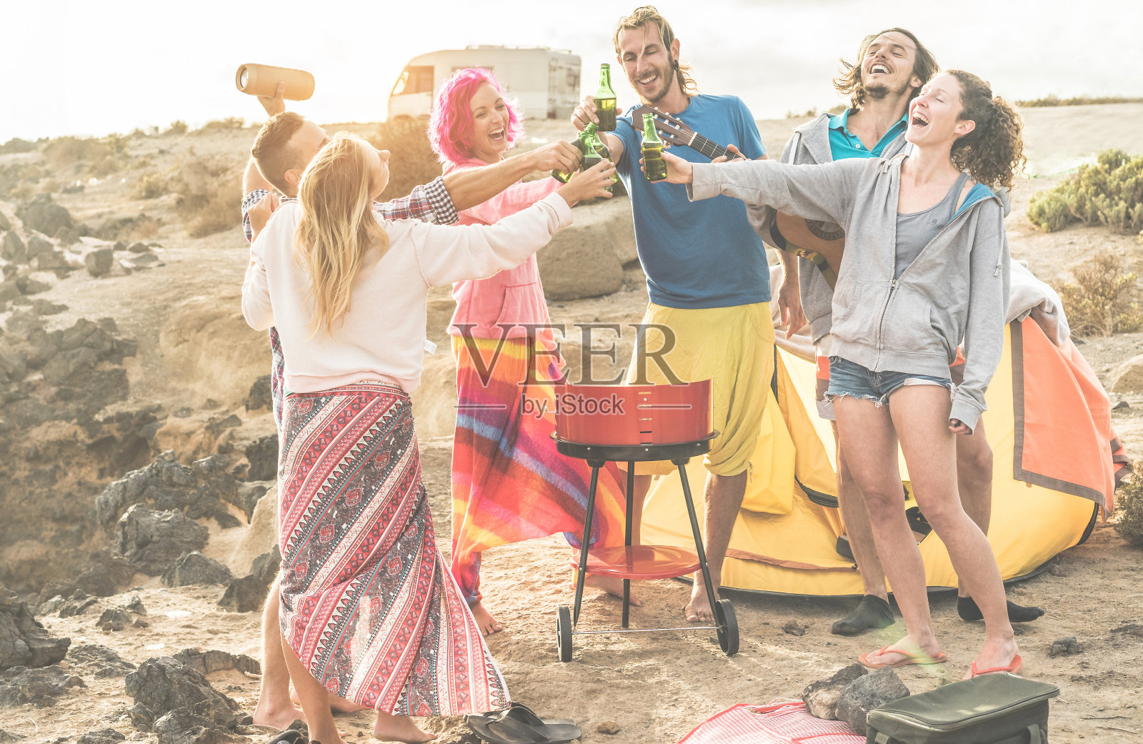 一群快乐的朋友欢呼与啤酒在露营在日落-时髦的人有乐趣玩音乐和大笑一起与货车在背景-旅行，度假，派对和友谊的概念照片摄影图片