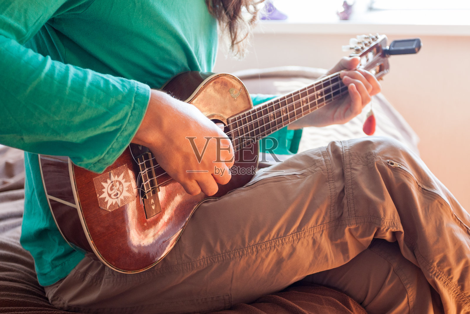 一个年轻人的手在家里弹奏一种木吉他尤克里里的特写。男人抱着尤克里里琴照片摄影图片