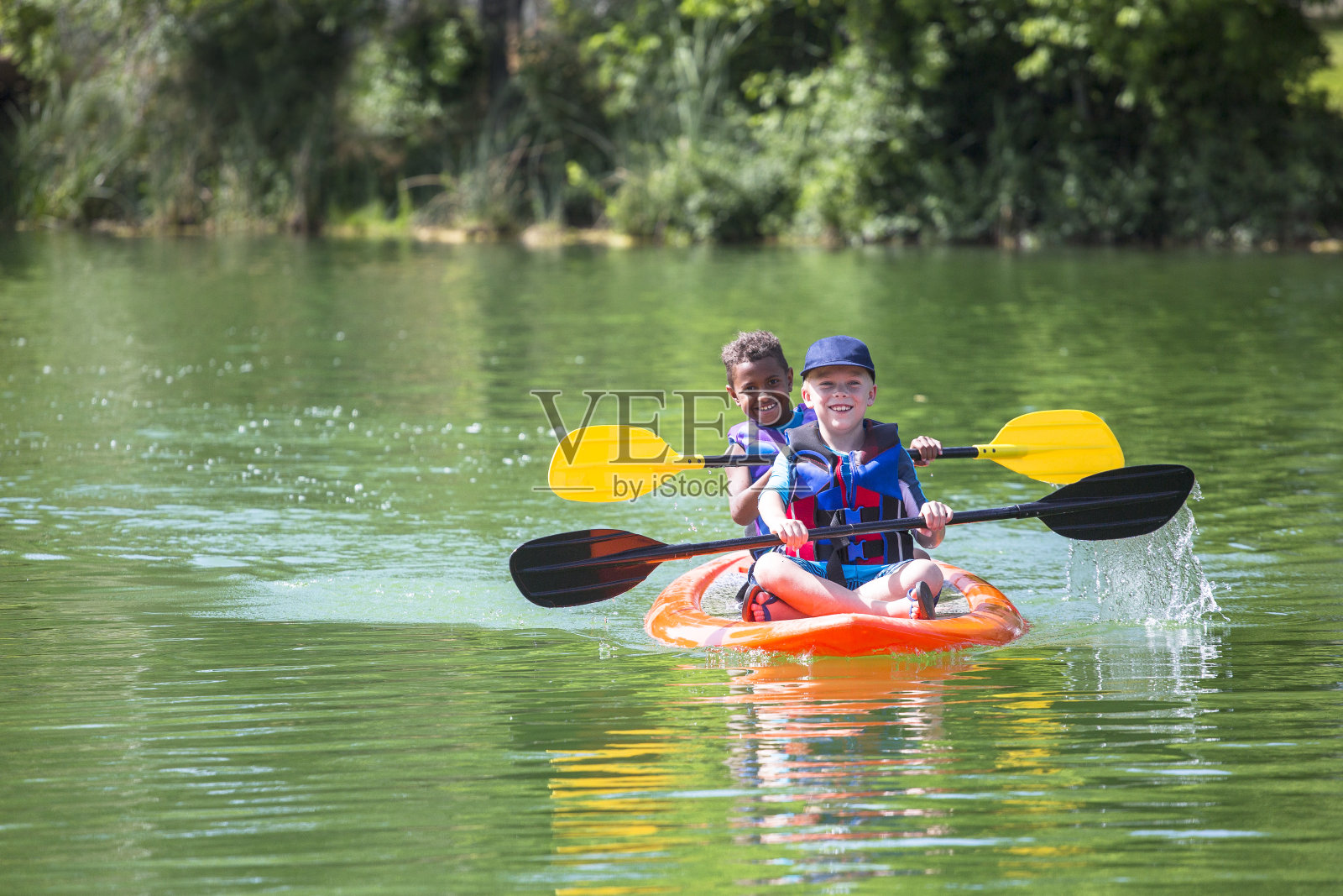 两个不同的小男孩在一条美丽的河里划皮划艇照片摄影图片
