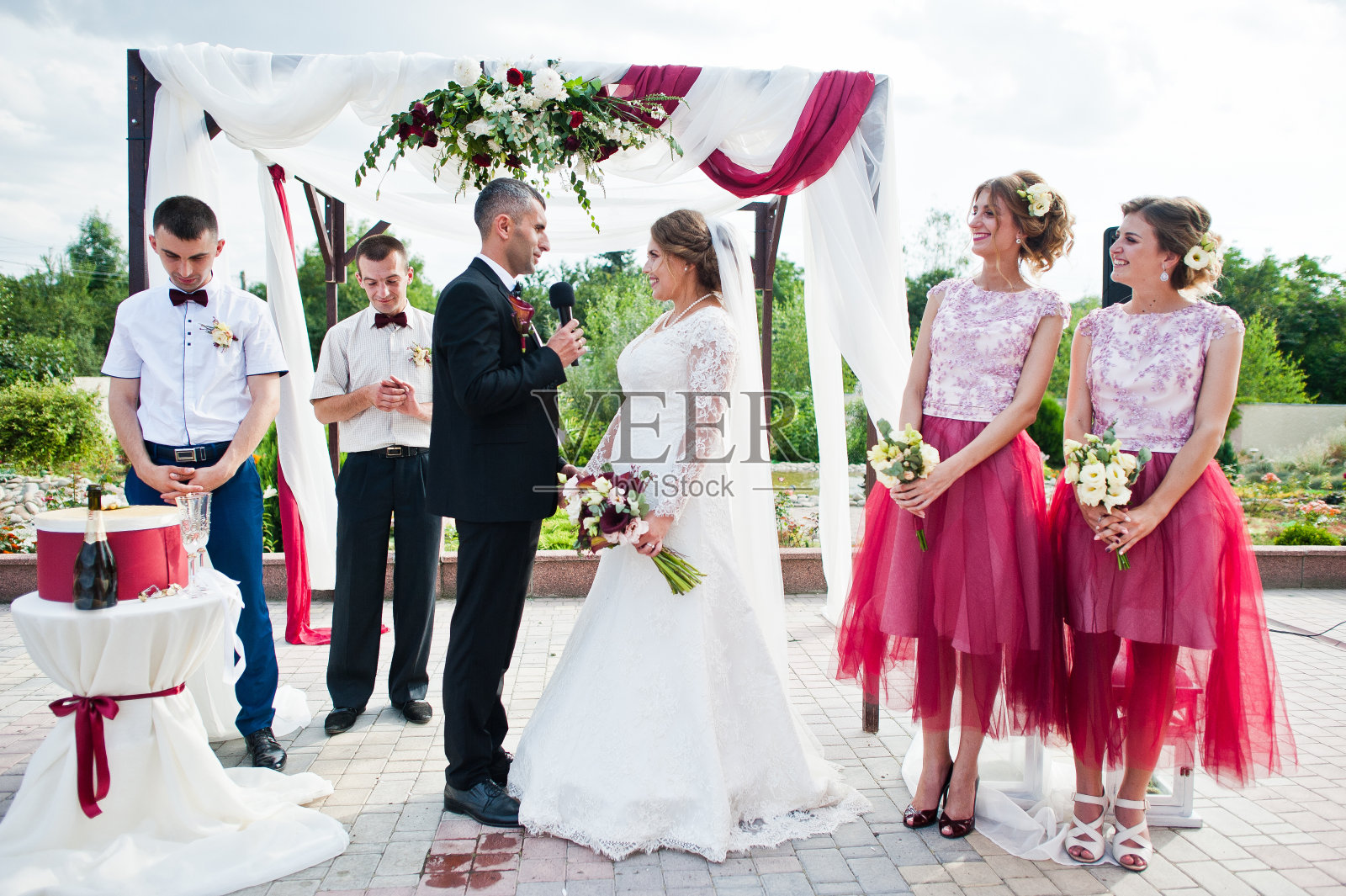 婚礼新人在众多宾客面前，在户外的花艺拱门下宣誓。照片摄影图片