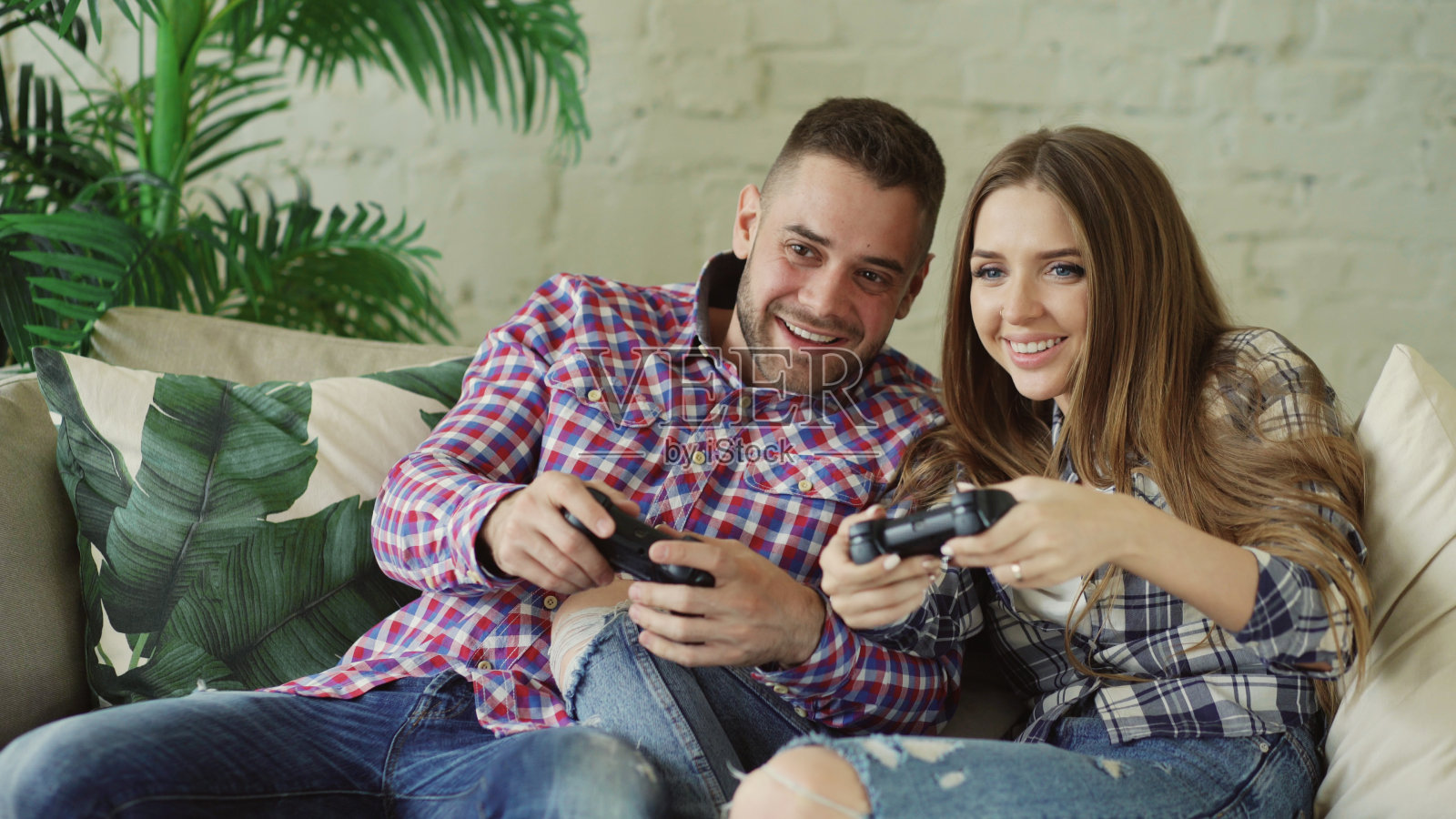 年轻的幸福和相爱的夫妇玩主机游戏与手柄，并有乐趣坐在客厅的沙发上照片摄影图片