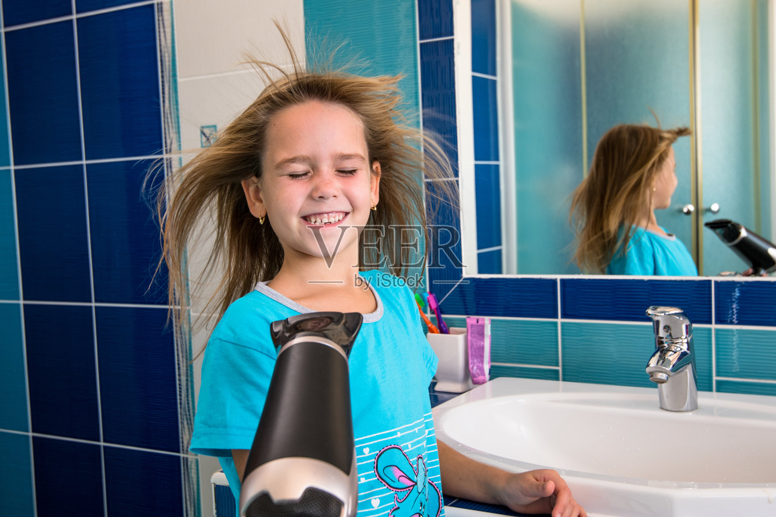 一个小女孩在浴室里用吹风机吹头发。照片摄影图片