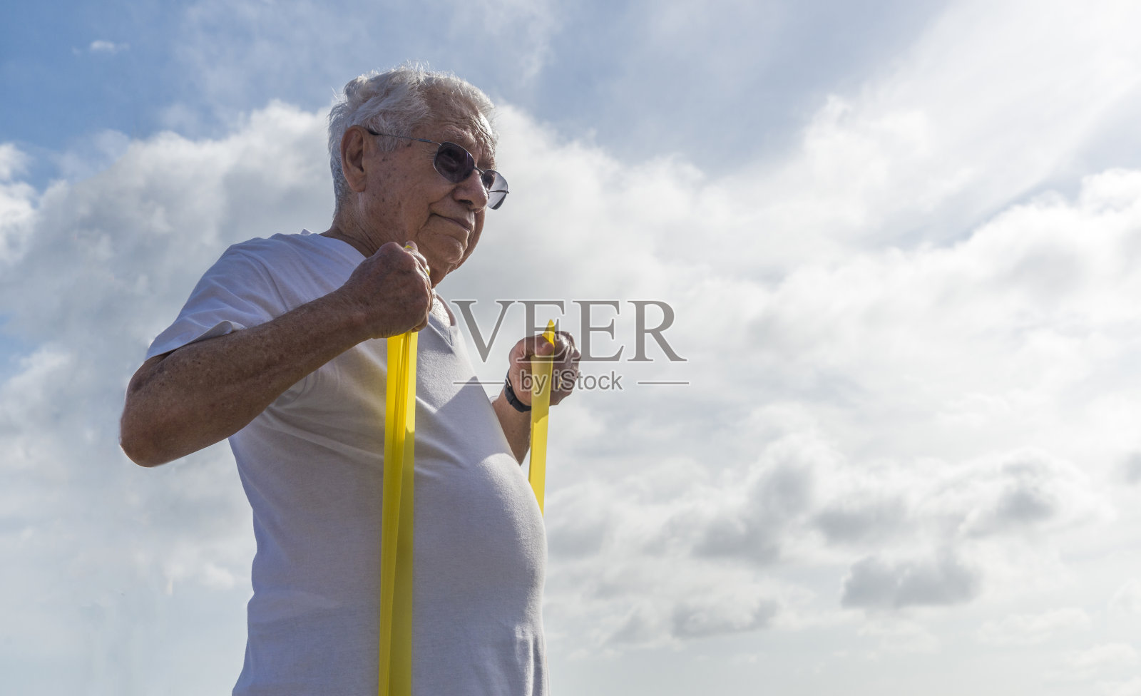 一名老人(80-89岁)在巴西里约热内卢伊帕内玛海滩的露天健身房用一根弹力绳锻炼照片摄影图片