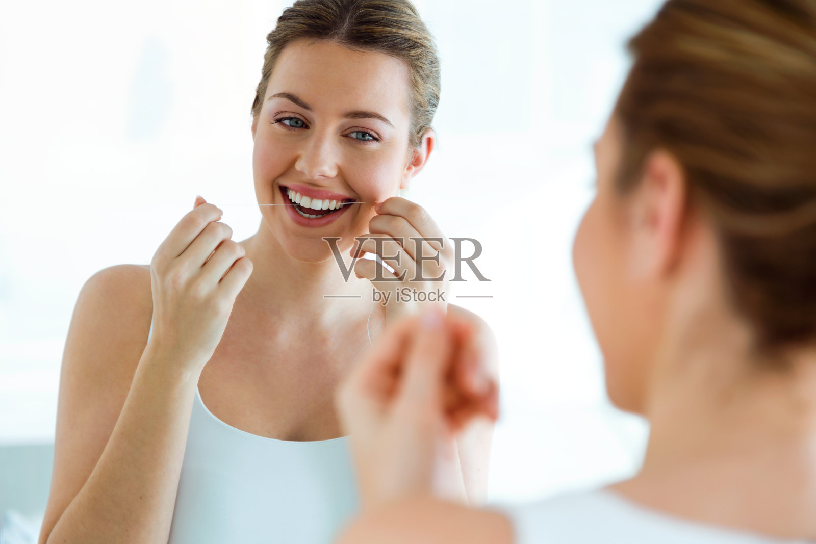 一个年轻漂亮的女人在家里的浴室里用牙线。照片摄影图片