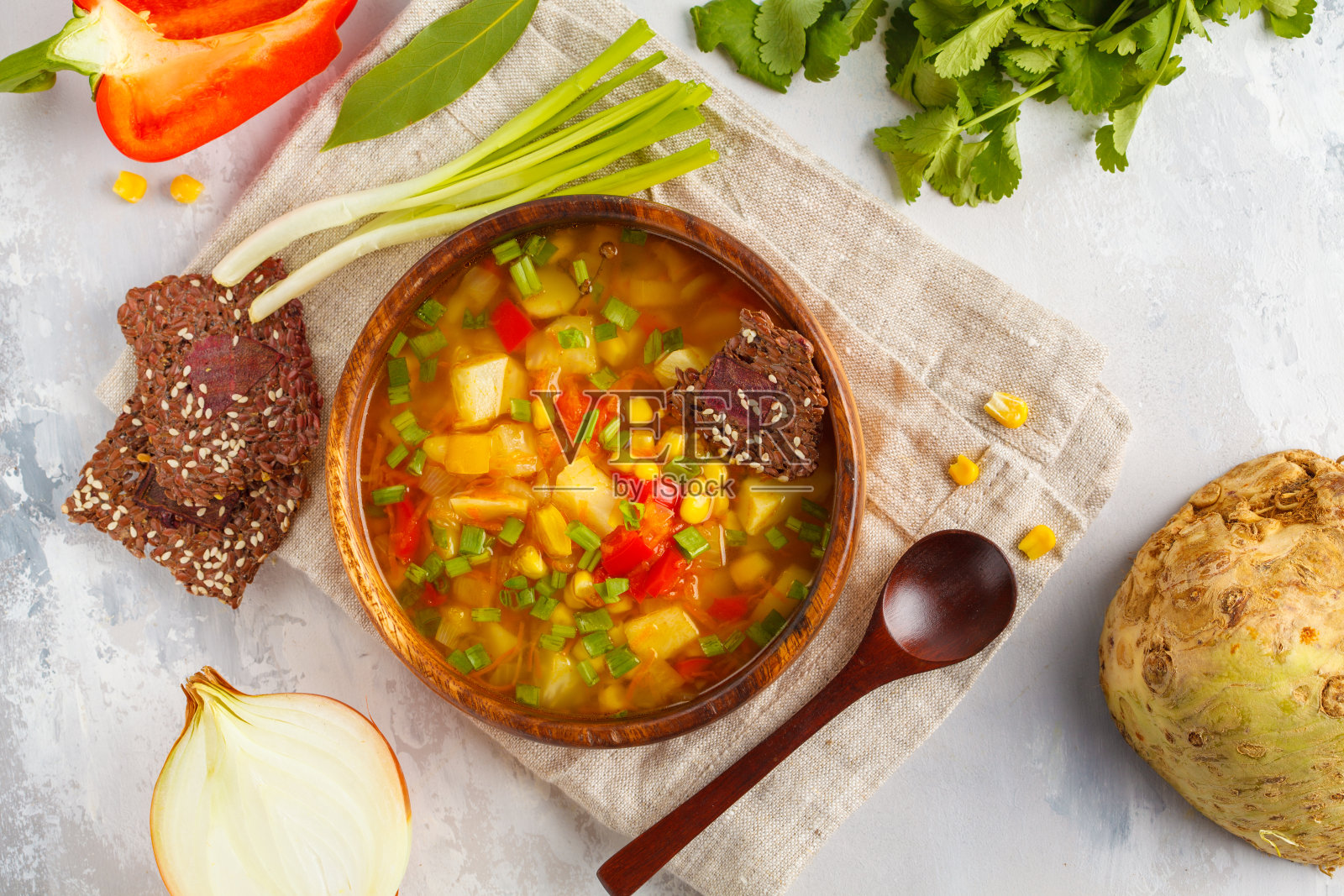 健康明亮的蔬菜玉米汤与芹菜根，胡椒，一个洋葱在一个木碗和亚麻脆面包。素食健康食品概念。照片摄影图片