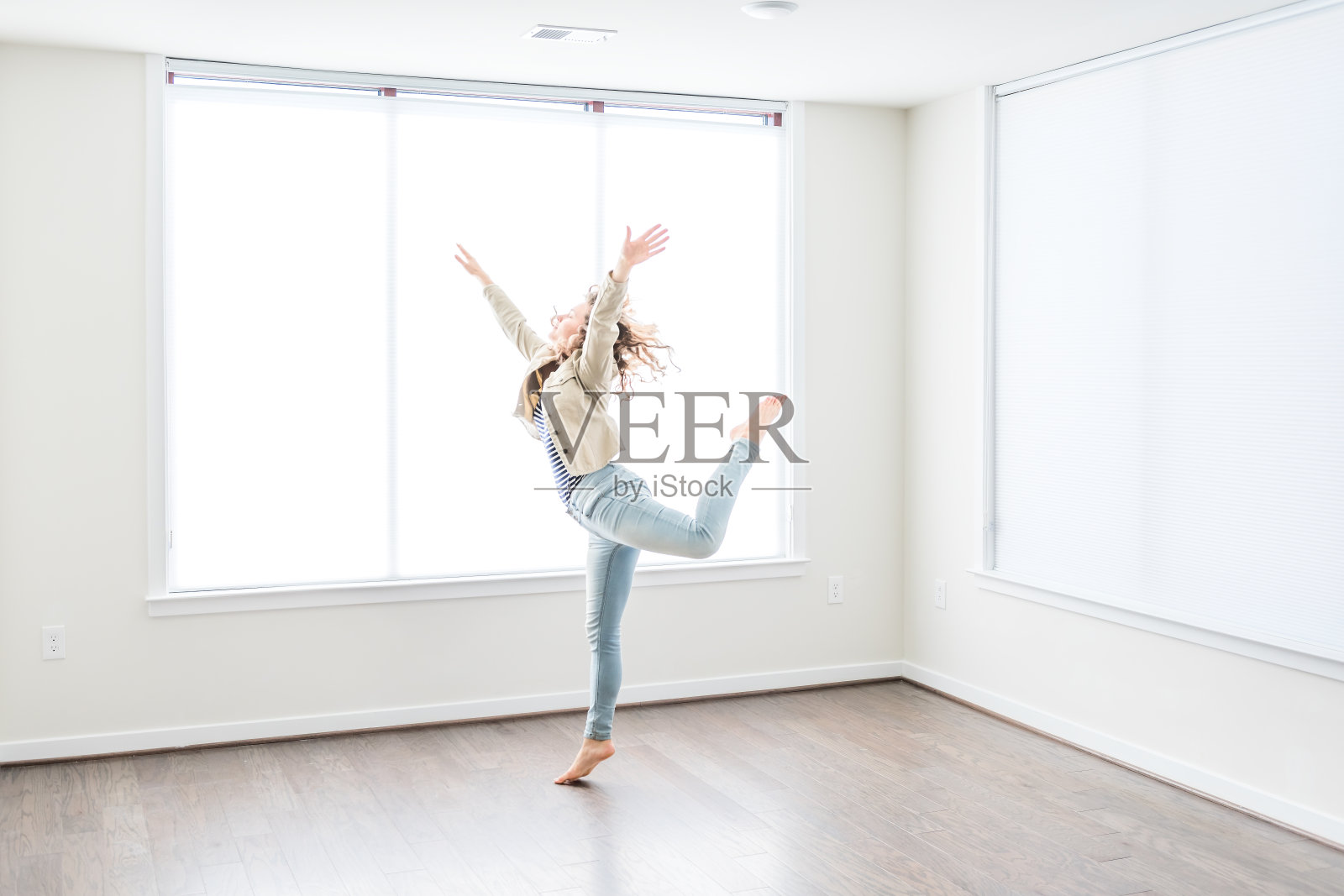 一个年轻快乐的女人跳在空的现代的新房间硬木地板和大阳光窗户公寓照片摄影图片