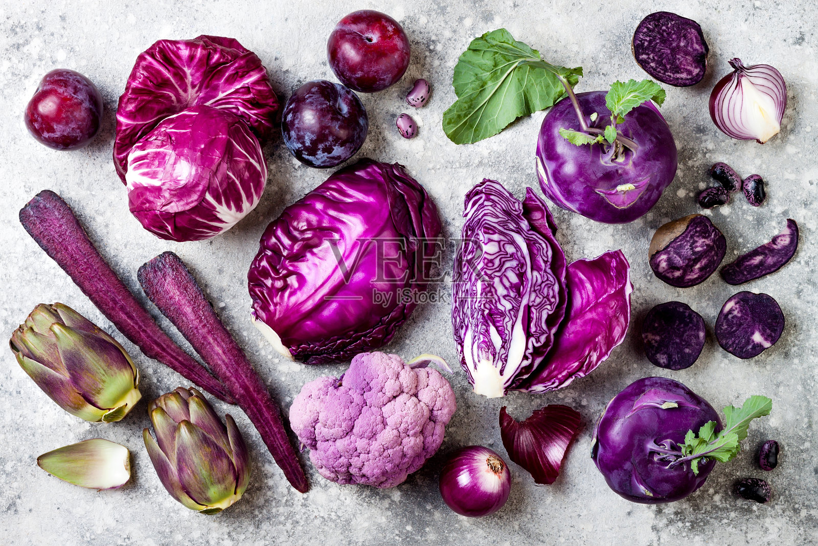 灰色混凝土背景上的紫色蔬菜。卷心菜，菊苣沙拉，橄榄，大头菜，胡萝卜，花椰菜，洋葱，洋蓟，豆类，土豆，李子。俯视图，平放。照片摄影图片