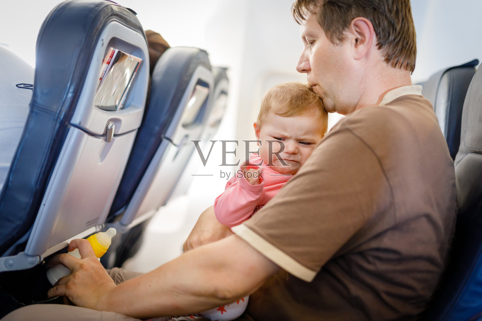 年轻疲惫的父亲和他哭闹的女儿在飞机上度假照片摄影图片