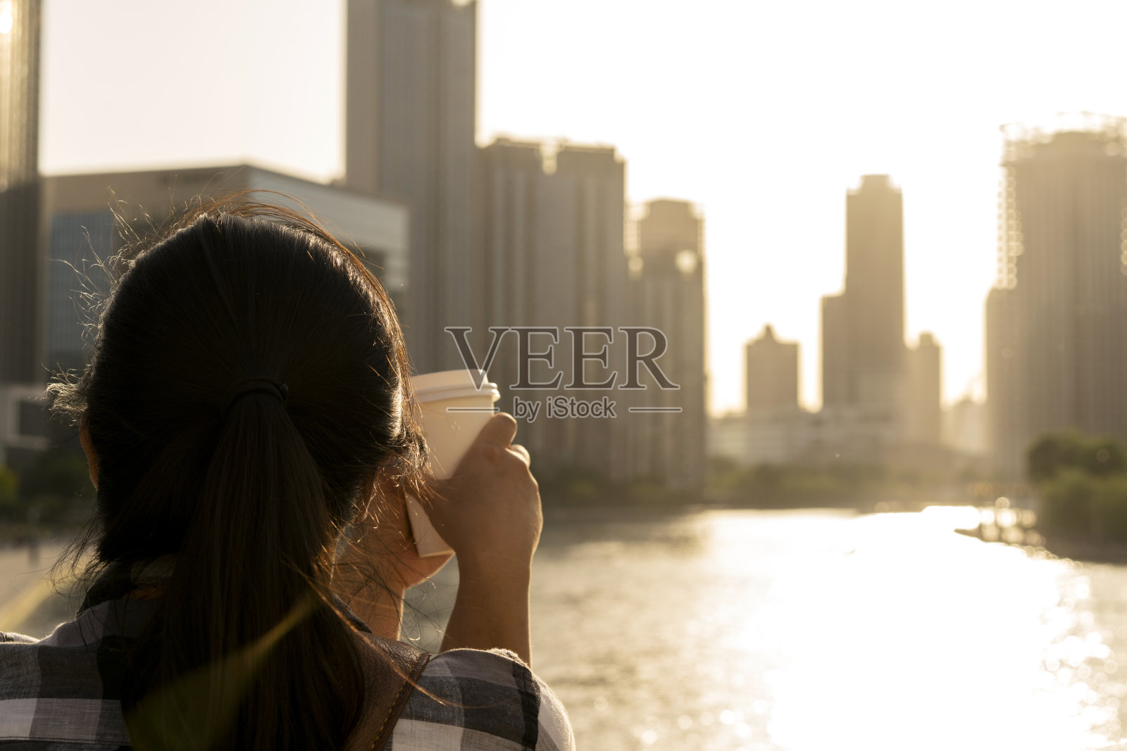 拿着咖啡杯的女孩，欣赏着夕阳下的城市天际线照片摄影图片