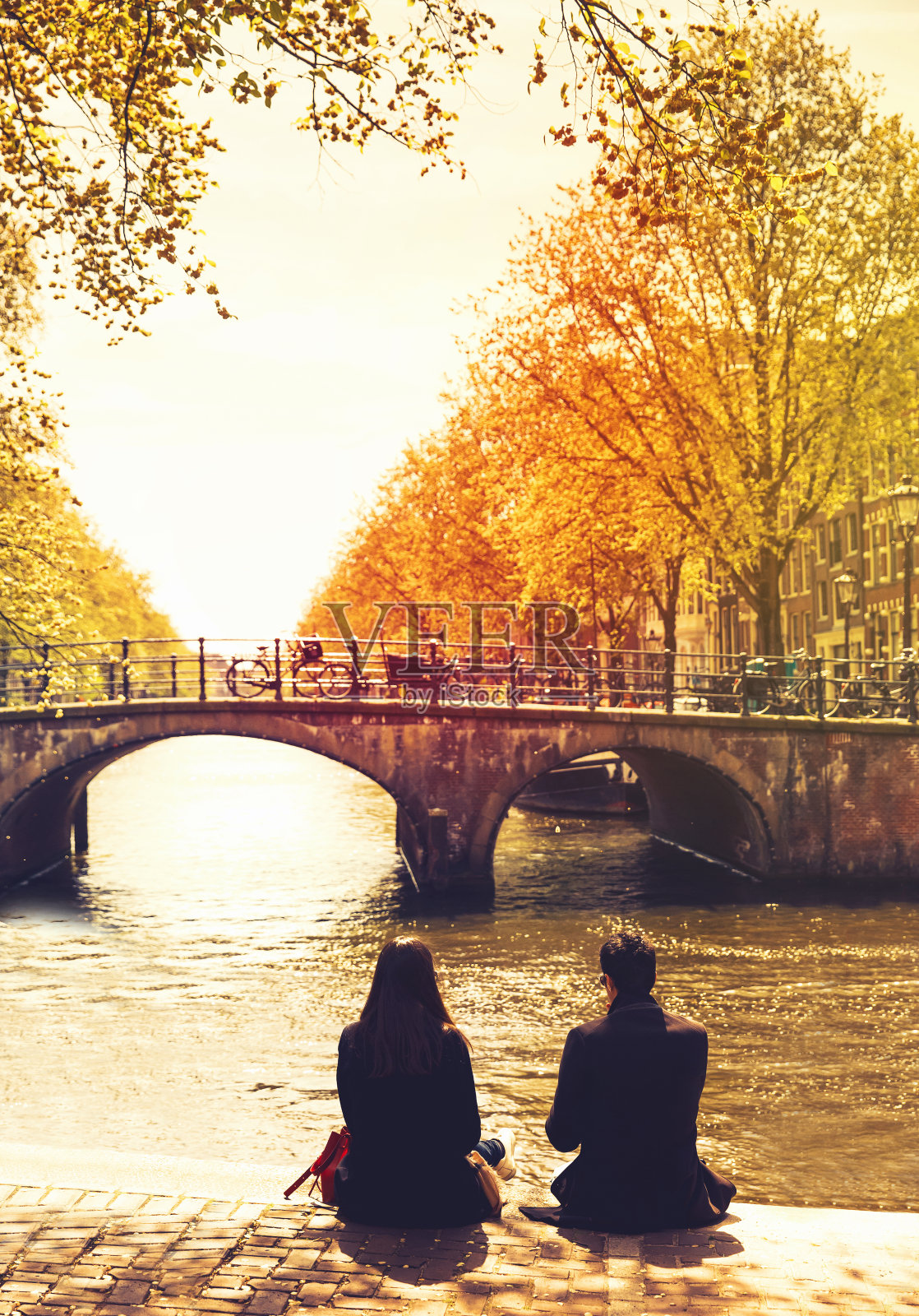 一对对朋友或恋人在运河的堤岸上放松，看着阿姆斯特丹的河流和桥梁。照片摄影图片