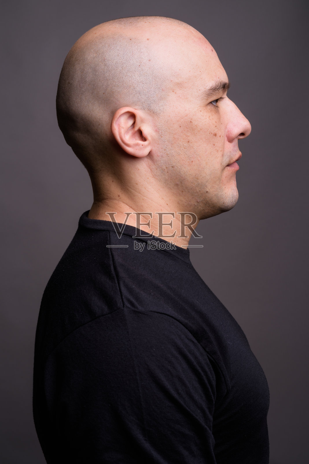 摄影棚里的一个肌肉发达的秃顶男人穿着黑色衬衫，背景是灰色照片摄影图片