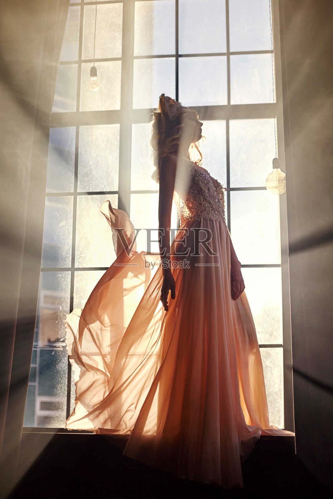 阳光下，穿着长裙的妇女站在窗前。童话公主女王照片摄影图片