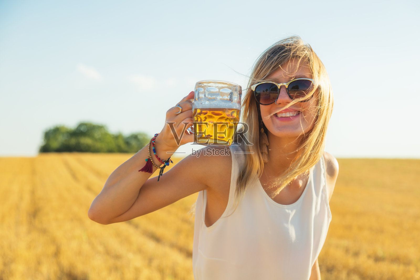 快乐的女孩拿着啤酒杯在一大片麦田里。照片摄影图片