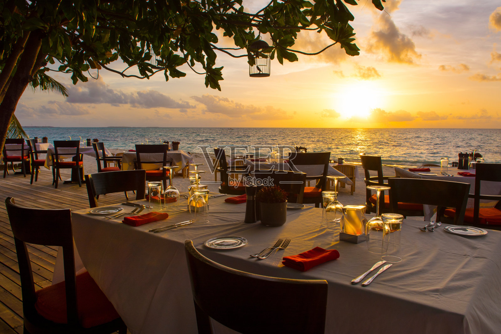 沙滩上的热带餐厅。美丽的日落景观在马尔代夫岛与多彩的天空和戏剧性的云在波浪的海。照片摄影图片