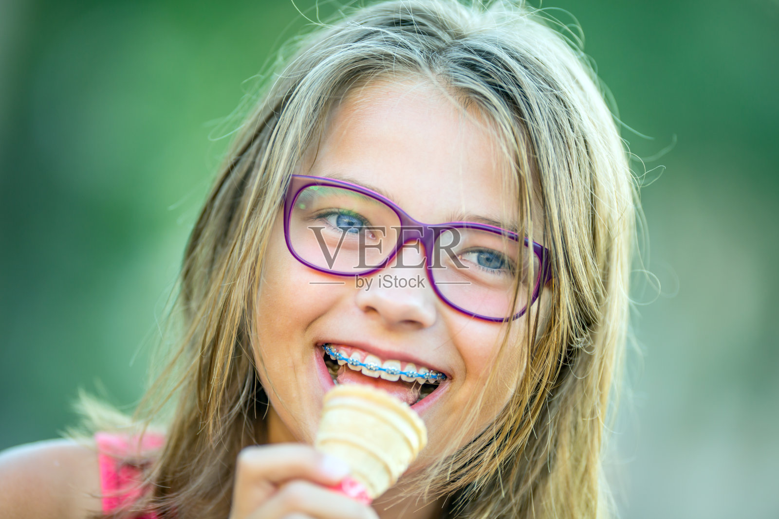 快乐的微笑女孩戴着牙套和眼镜。年轻可爱的白种金发女孩戴着牙套和眼镜照片摄影图片