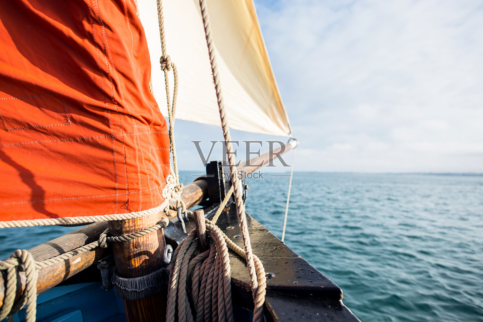 缠绕在木夹板上的绳子固定在一艘有米色三角帆和赭色帆的老式帆船的船体上照片摄影图片