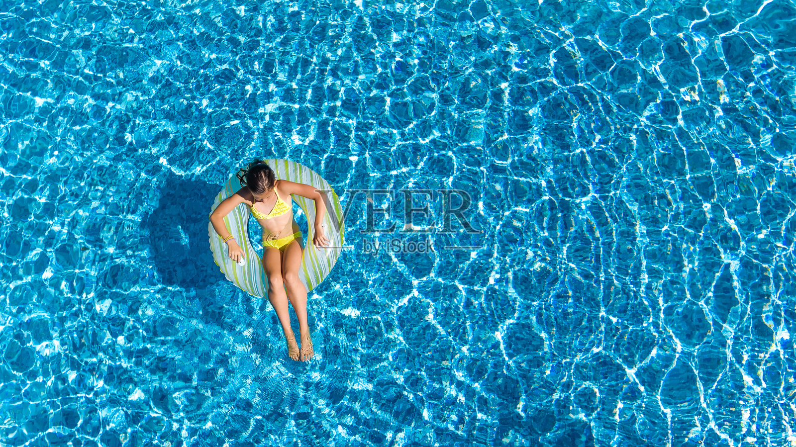 鸟瞰图的女孩在游泳池从上面，孩子游泳在充气圈甜甜圈和有乐趣的水在家庭度假照片摄影图片