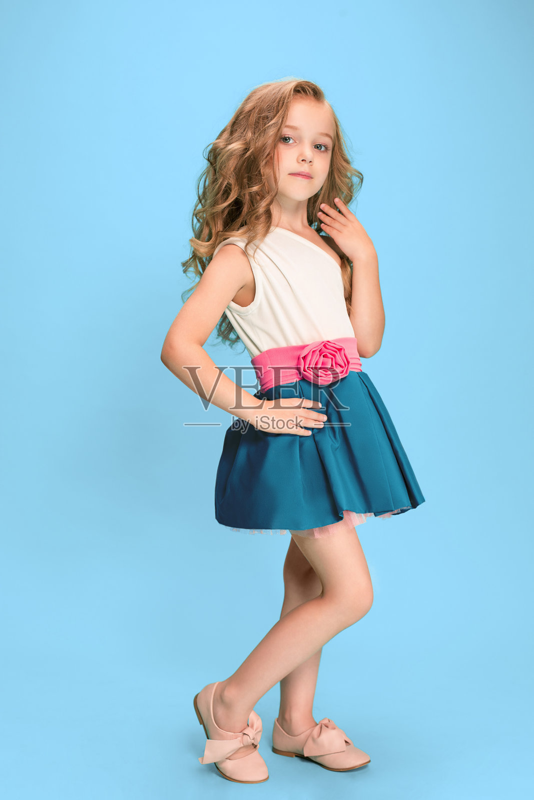 全长美丽的小女孩在连衣裙站和摆姿势在蓝色的背景照片摄影图片