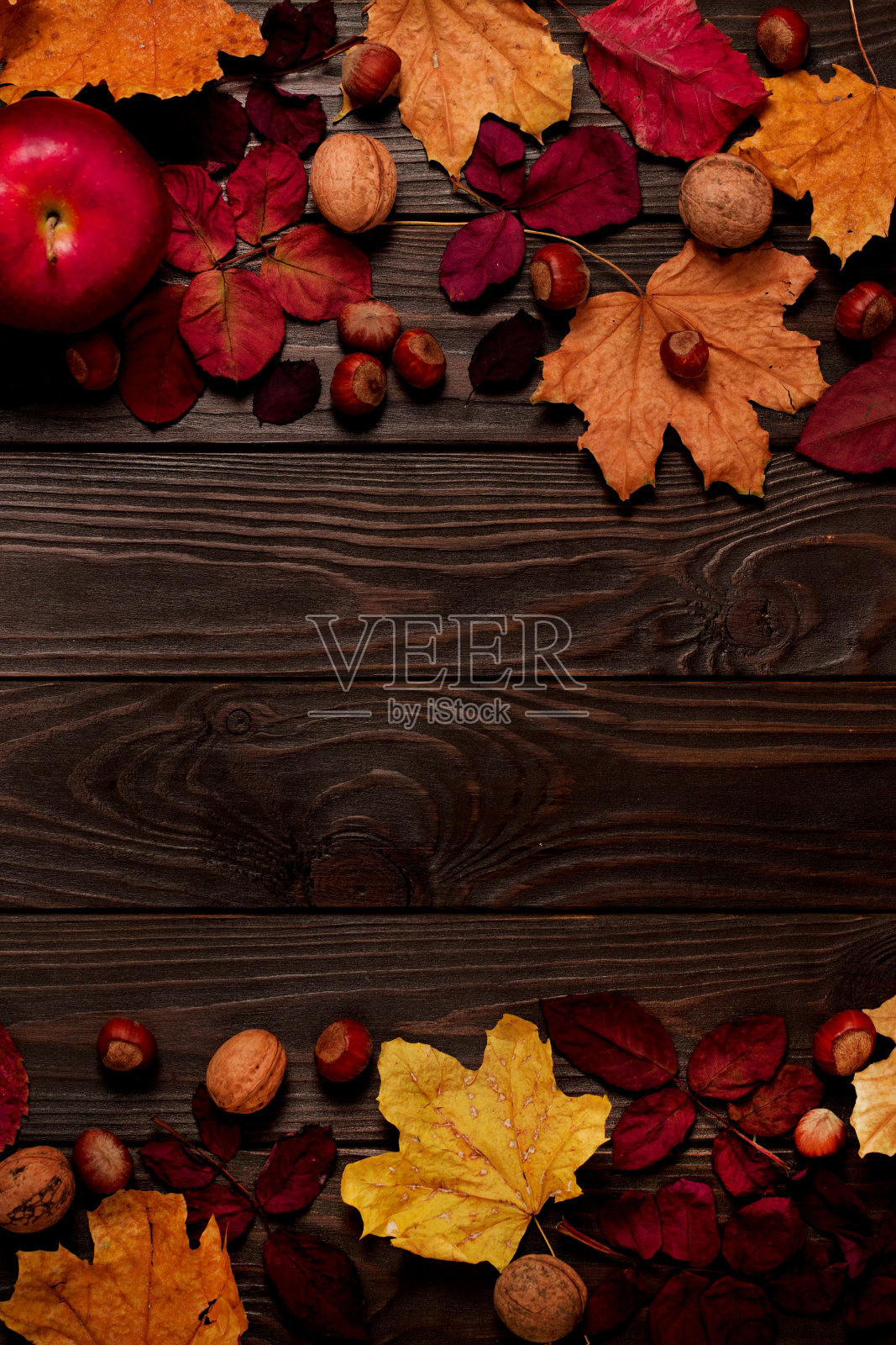 深红和黄色的秋叶、榛子、核桃和苹果在深色的木头背景上平铺成一幅框架。照片摄影图片