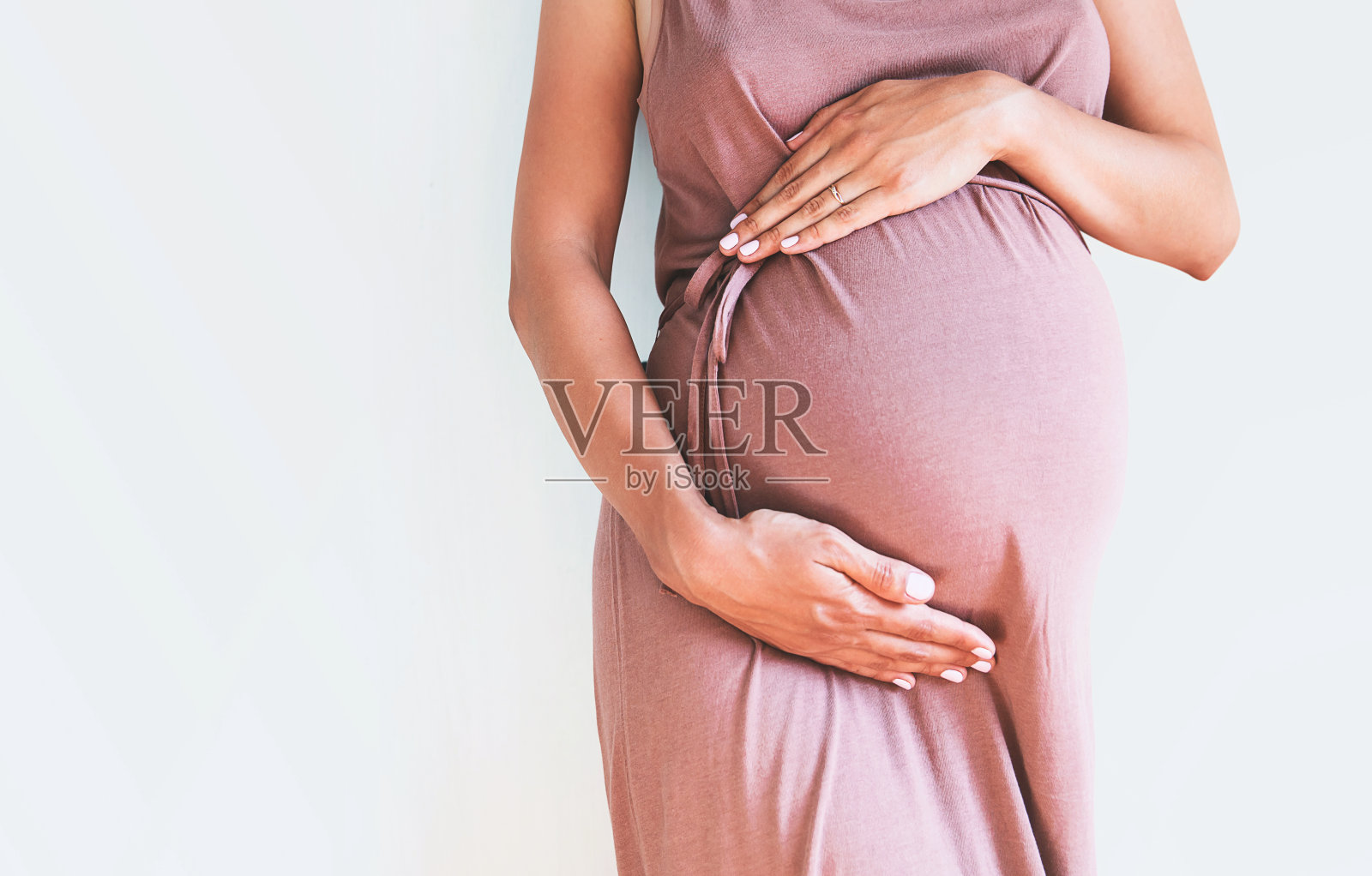 穿着礼服的孕妇双手放在白色背景上的肚子上。照片摄影图片