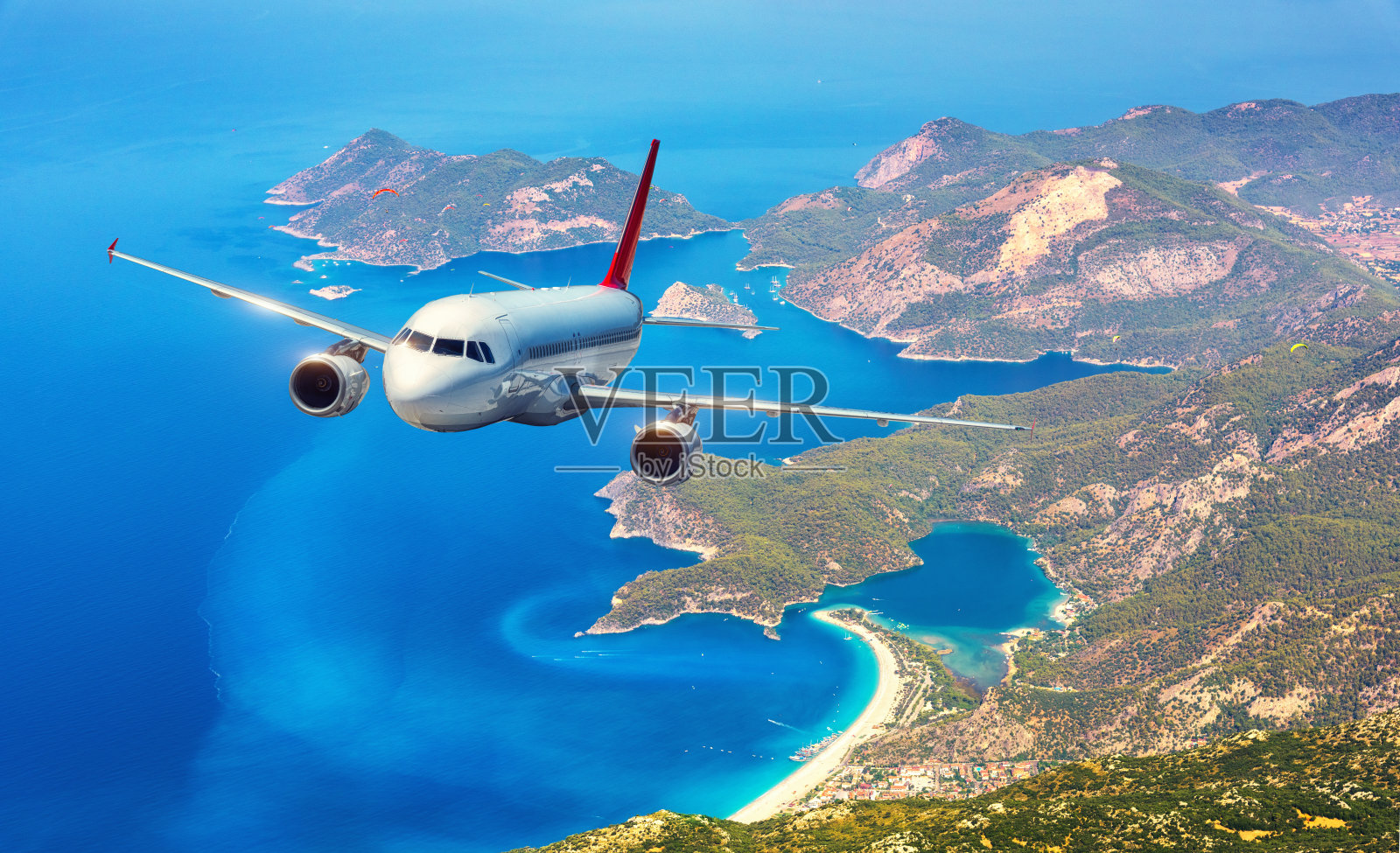 在晴朗的日子里，飞机在美丽的岛屿和地中海上空飞行。白色的客机，山脉和蓝色的水。客机。商务旅行。商用飞机照片摄影图片