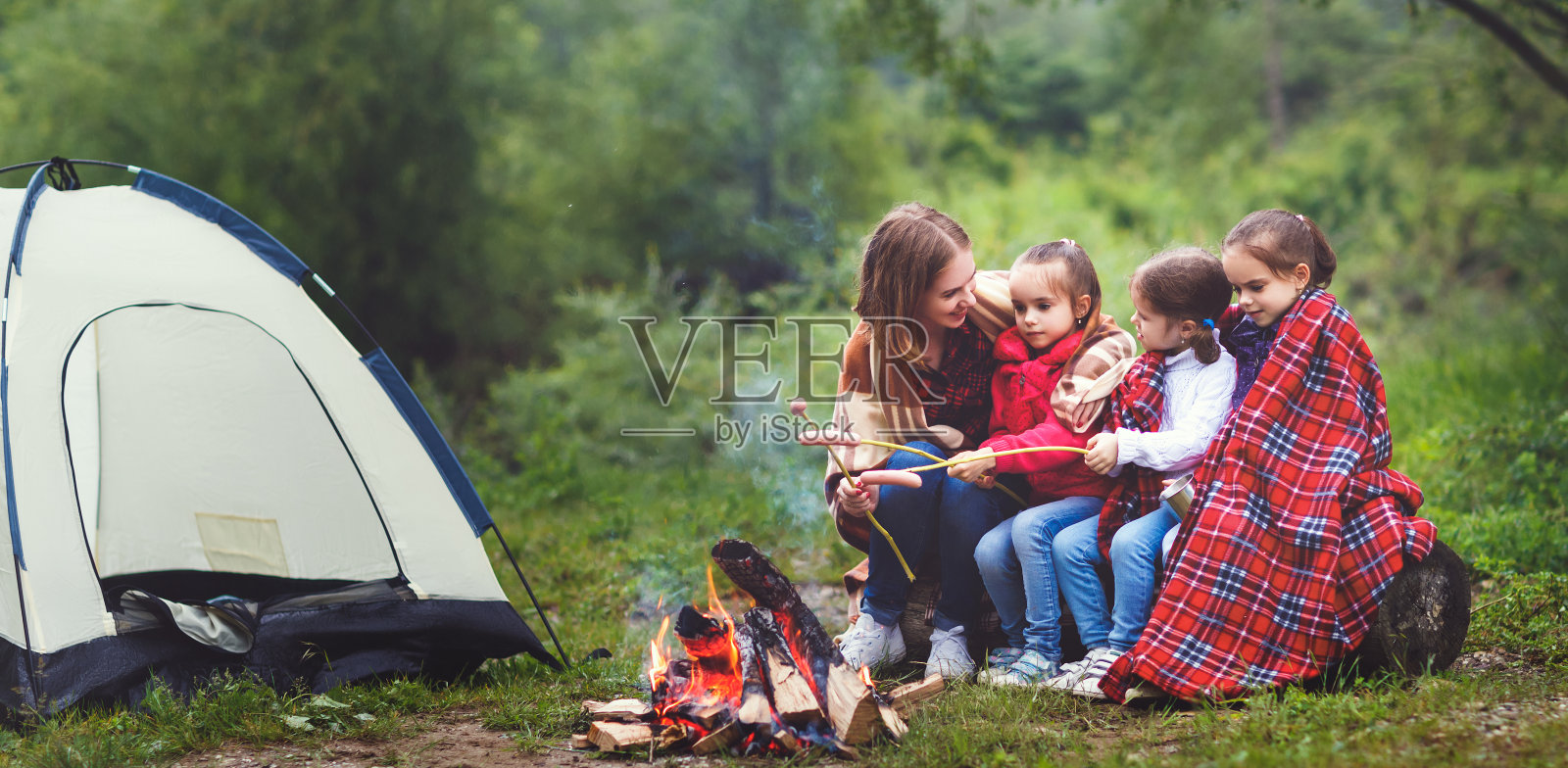 快乐旅游家庭旅行徒步。妈妈和孩子们在帐篷附近的篝火上煎香肠照片摄影图片