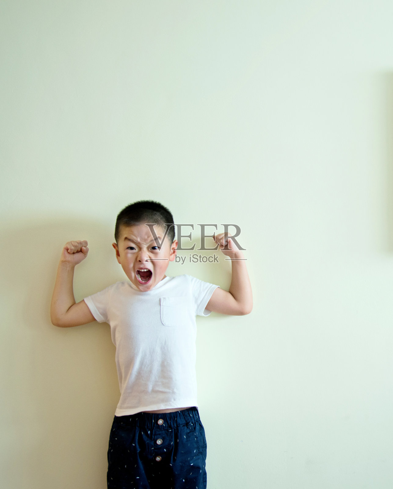 小男孩靠墙站着，露出他的肌肉照片摄影图片
