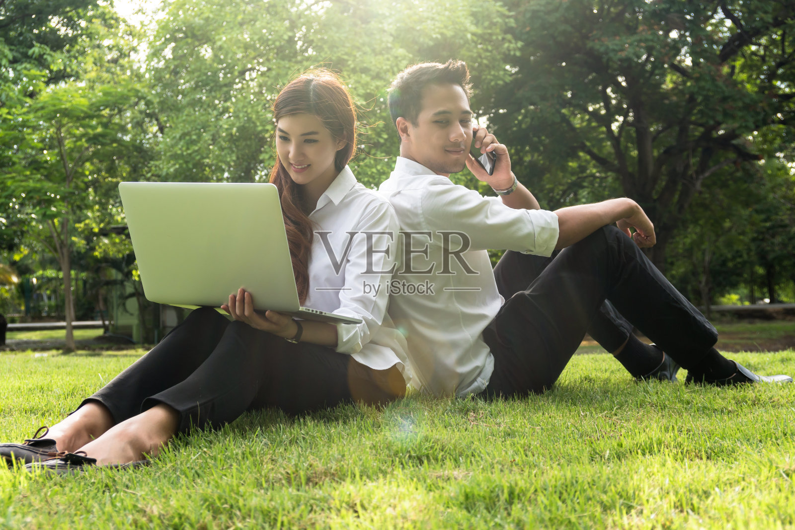 快乐的亚洲夫妇大学工作与科技笔记本电脑和通过智能手机在公园与镜头光晕，商业和生活方式的概念照片摄影图片