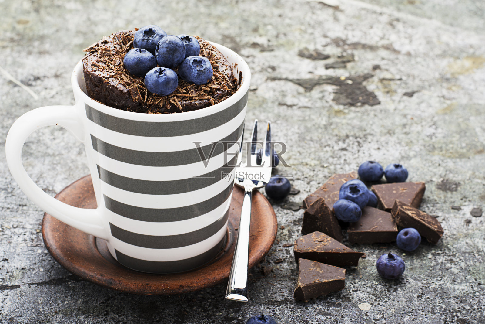 健康的早餐或零食。灰色的石头背景上的灰色条纹陶瓷杯子里有蓝莓和巧克力片的巧克力杯蛋糕。有选择性的重点。照片摄影图片