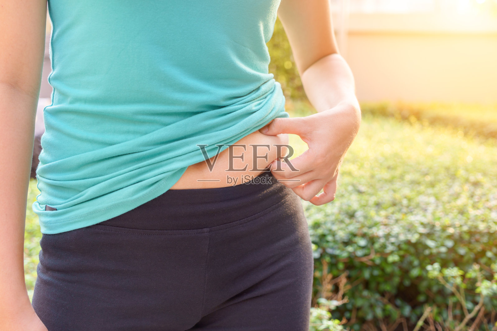 胖乎乎的女人手握着自己的大肚子在户外的阳光下。照片摄影图片