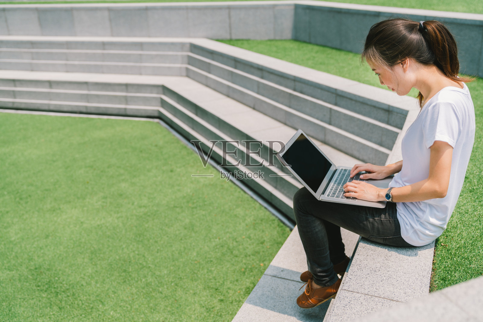 亚洲大学生或自由职业女性在大学校园或现代公园的楼梯上使用笔记本电脑。信息技术、教育或休闲业务概念。拷贝空间在绿色草地庭院照片摄影图片
