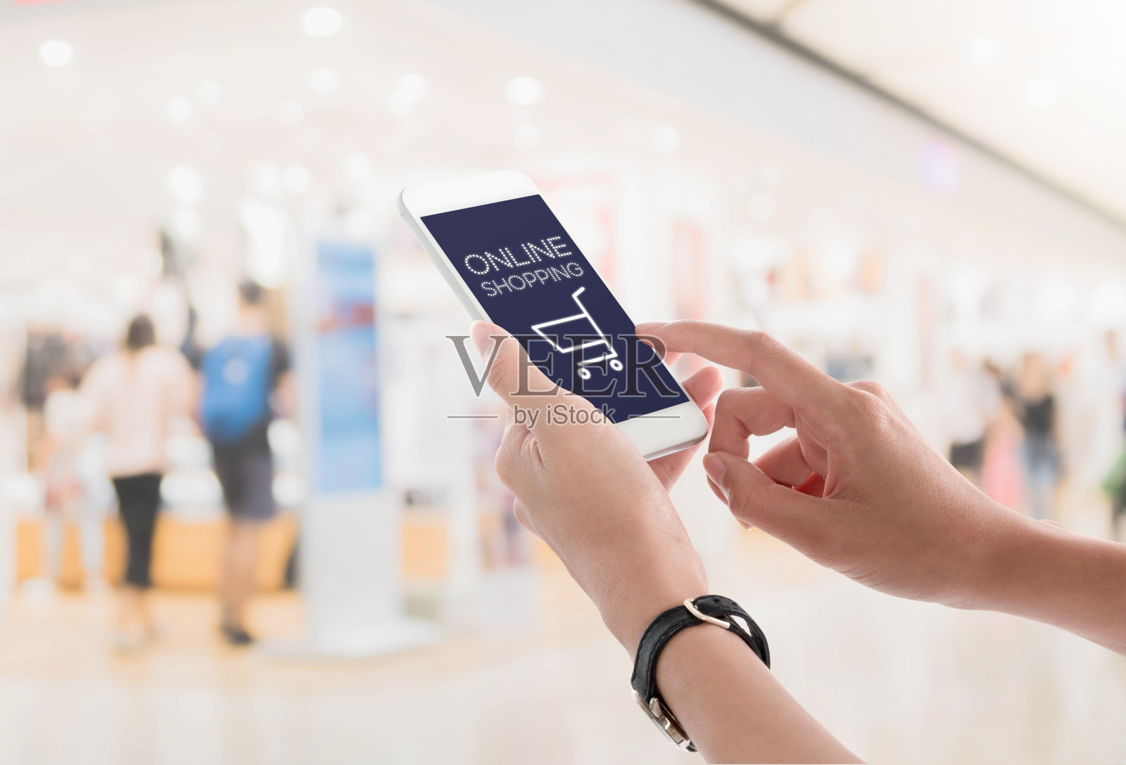 一个女人牵着手机购物，购物中心内部模糊的背景显示着购物屏幕。电子商务的概念。照片摄影图片