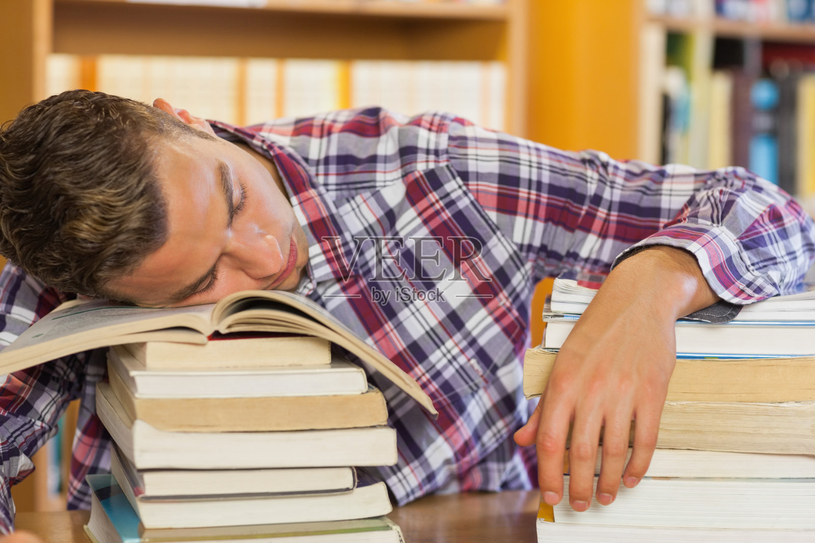 疲惫英俊的学生把头靠在成堆的书上休息照片摄影图片