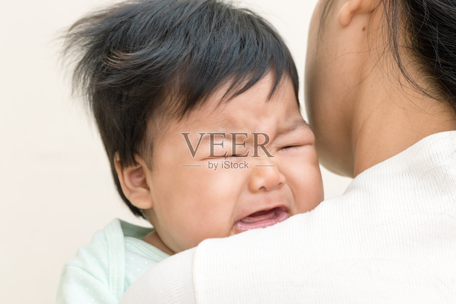可爱的亚洲婴儿生病，哭在妈妈的肩膀上。照片摄影图片