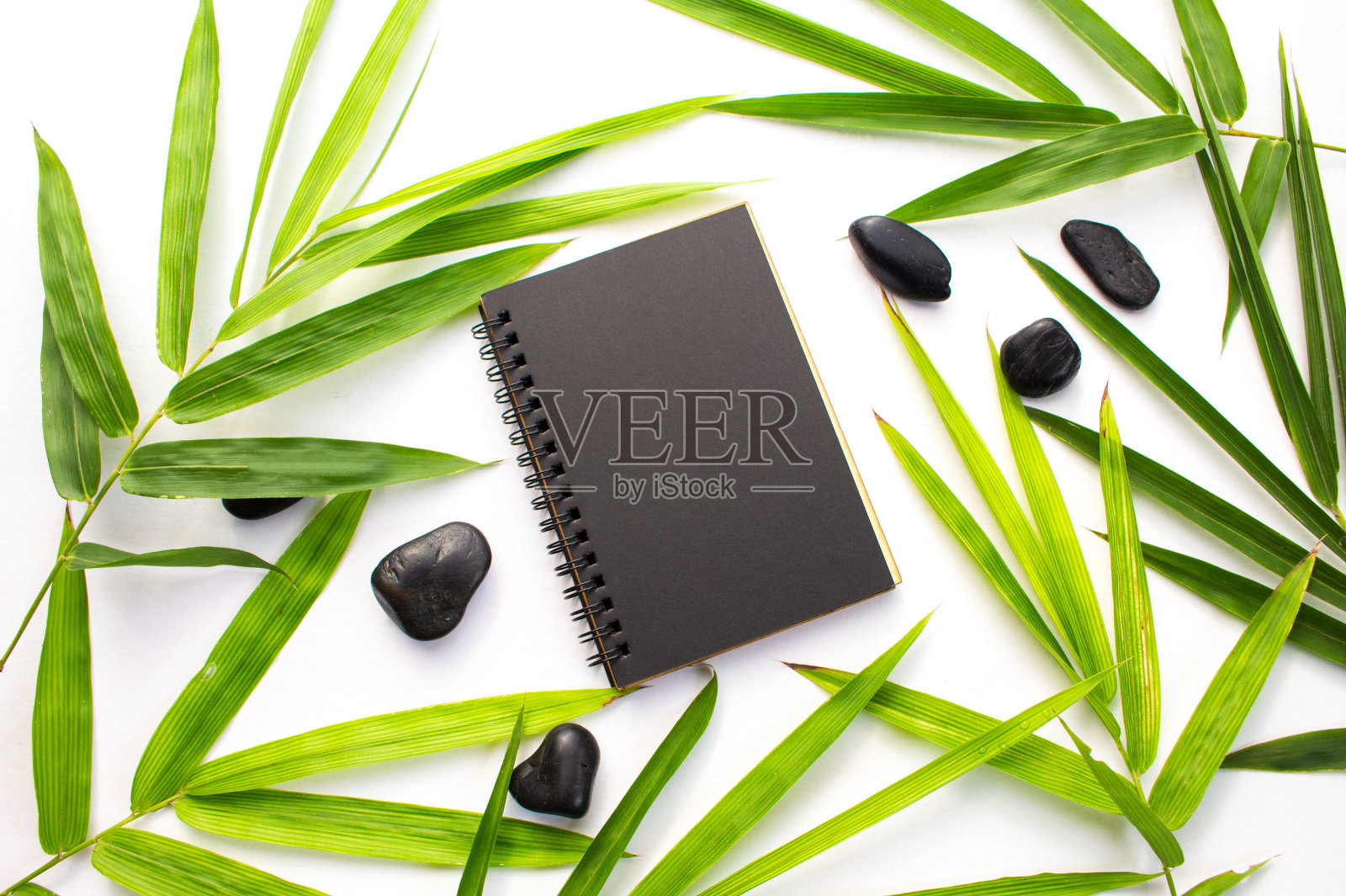 竹叶禅宗背景。黑色纸笔记本模型。翠绿的竹叶和沙滩卵石平铺着。照片摄影图片