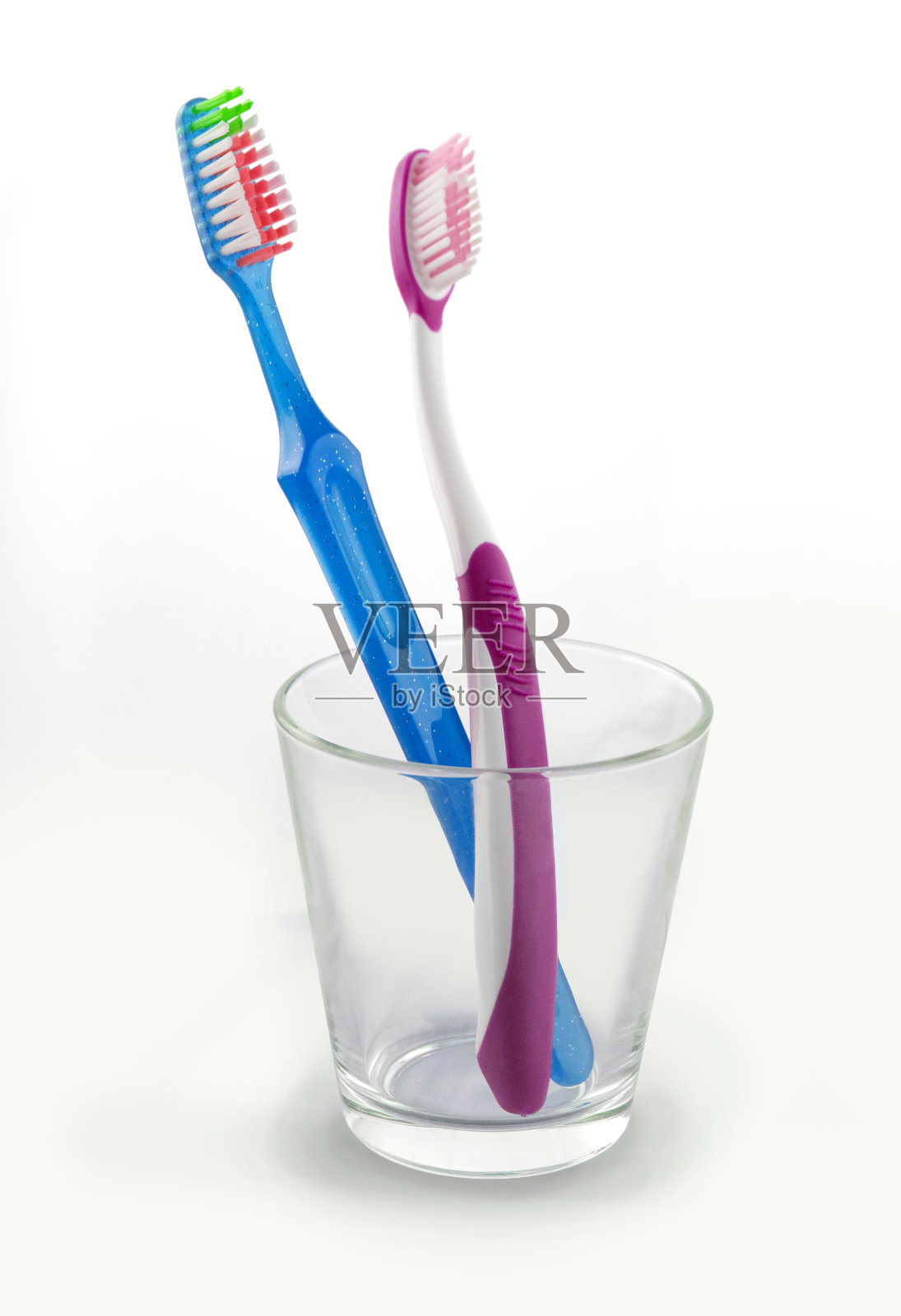 一只蓝色的牙刷，一只粉红色的装在玻璃杯里照片摄影图片