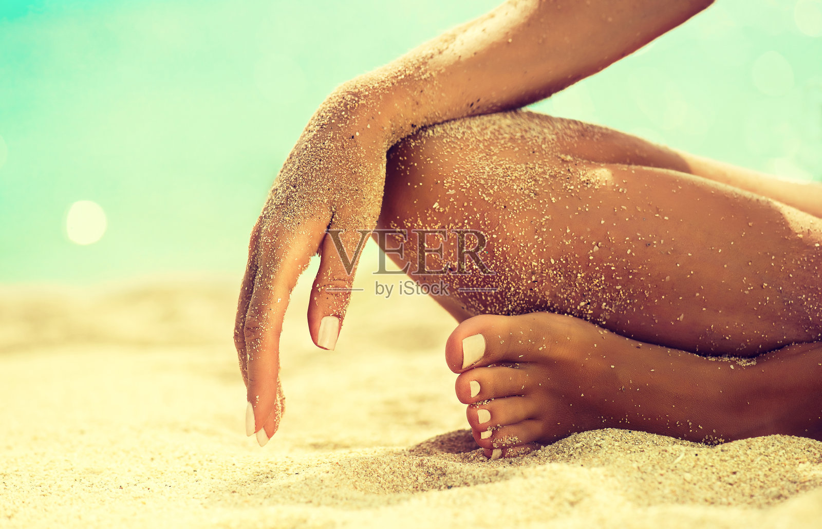 女人的手正躺在被海沙覆盖的膝盖上。照片摄影图片