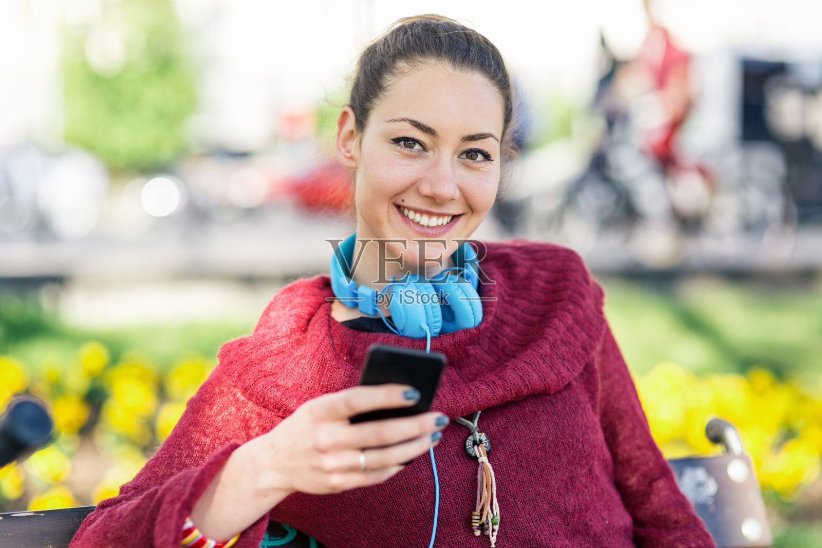 微笑的女性坐在户外长椅上，用手机发短信照片摄影图片
