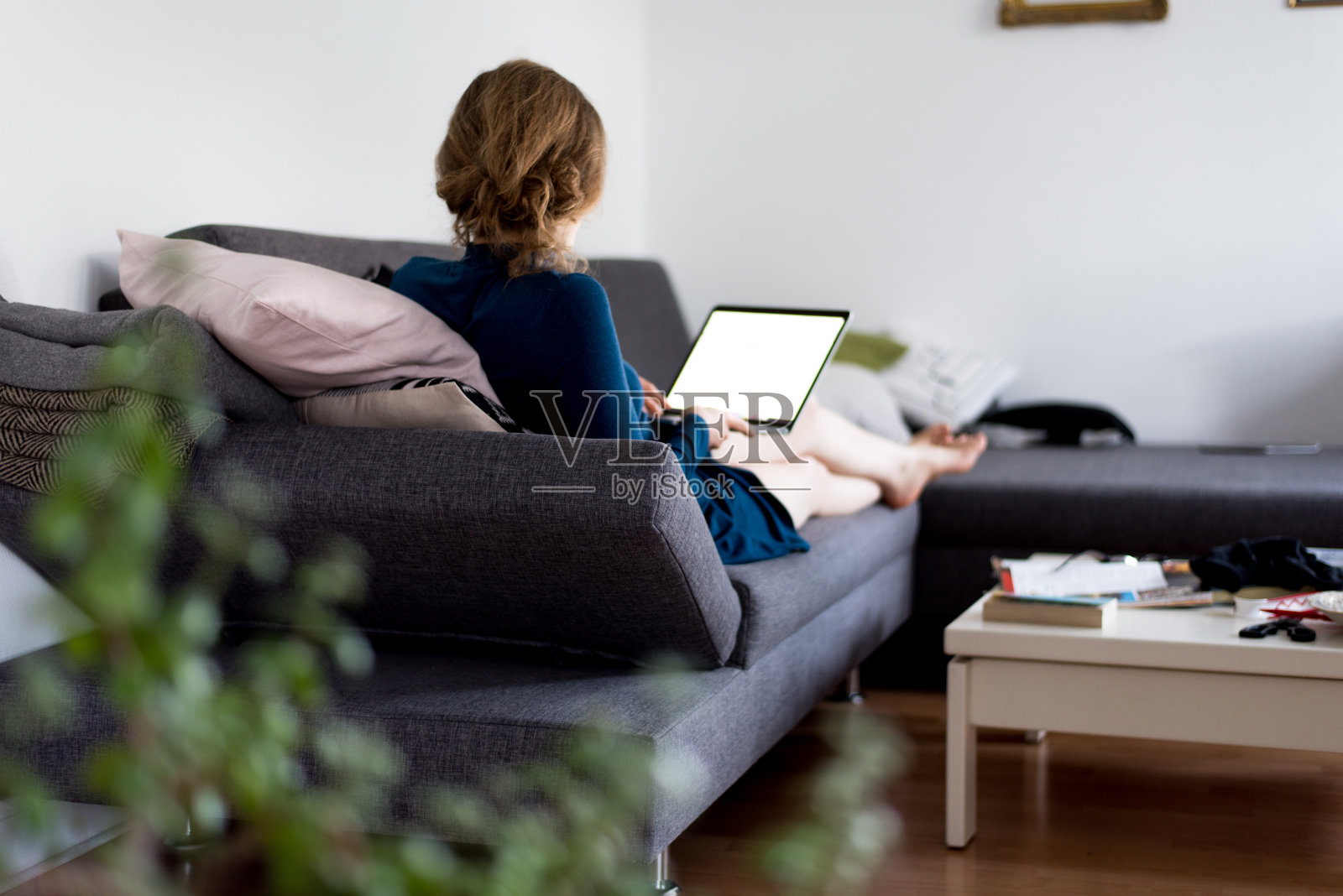 一个女人坐在家里的沙发上，在家里用笔记本电脑工作，屏幕是空白的照片摄影图片