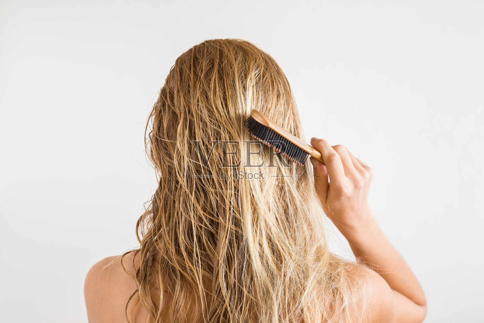 在灰色的背景上，一个女人用梳子梳着她淋湿的金发。关心健康清洁的头发。美容院的概念。照片摄影图片