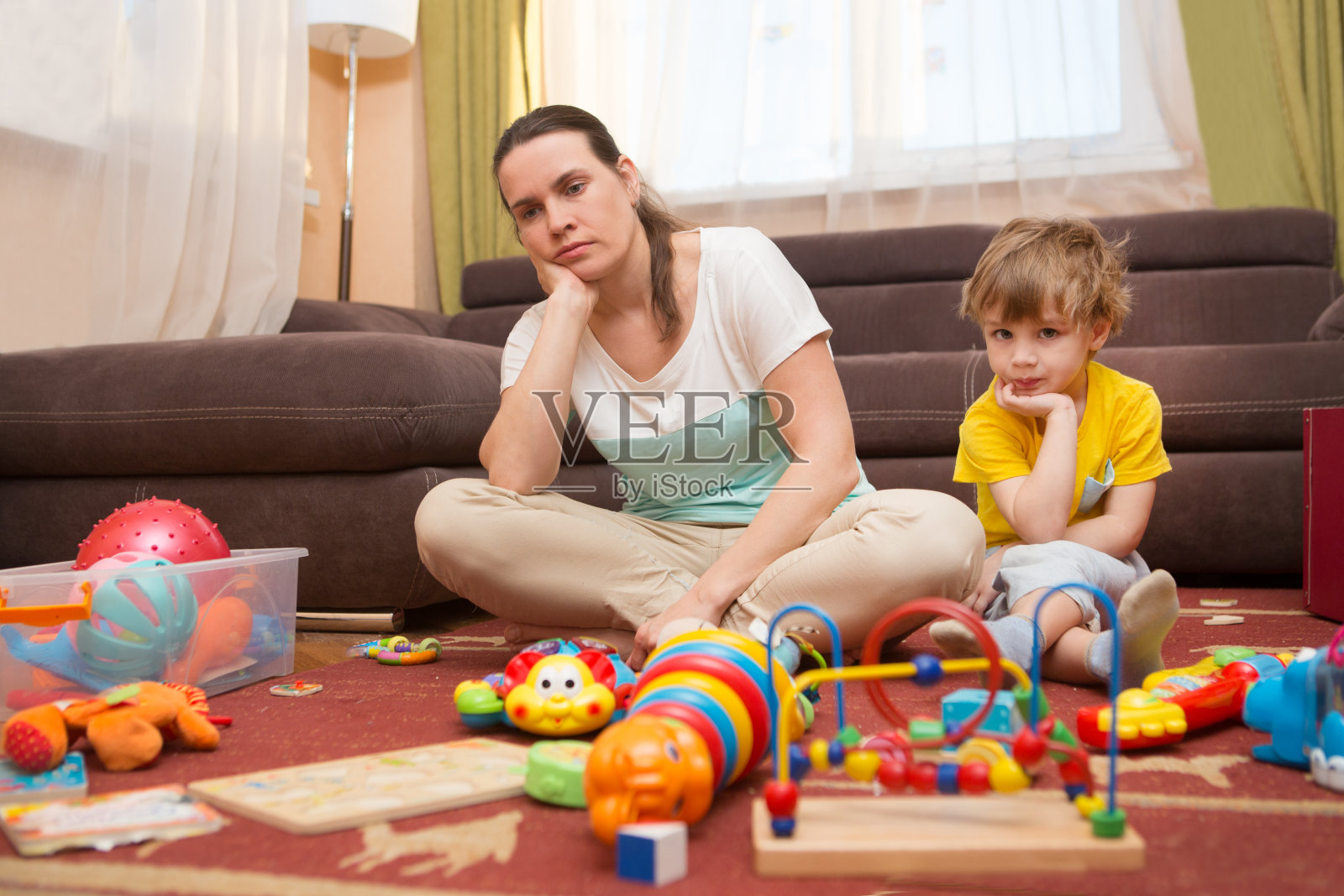 年轻的孕妇和她的小儿子，在家里。母亲和小儿子坐在地板上。妈妈努力整理房子。分散孩子的玩具。家里乱七八糟照片摄影图片