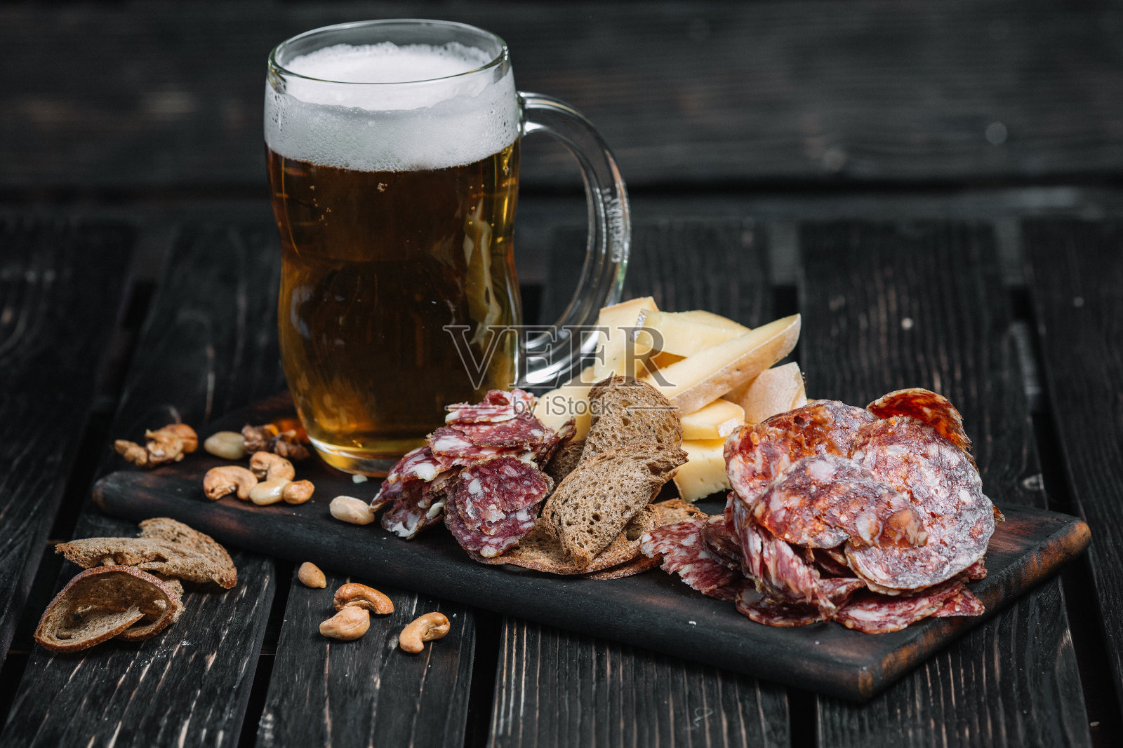 大杯啤酒和零食在木板上的深色木材背景。波兰熏肠，奶酪，坚果，吐司照片摄影图片