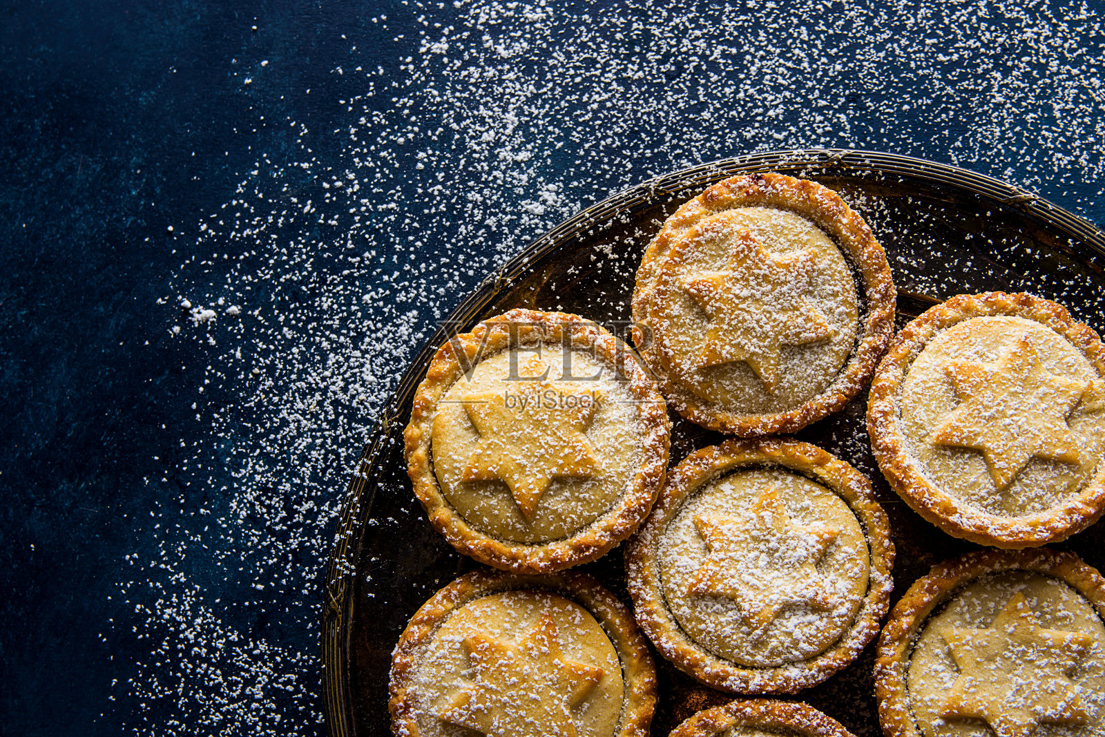 传统的英国圣诞糕点甜点家烤碎馅饼与苹果葡萄干坚果填充金色酥皮在复古金属板上粉末深蓝色雪背景顶视图拷贝空间照片摄影图片