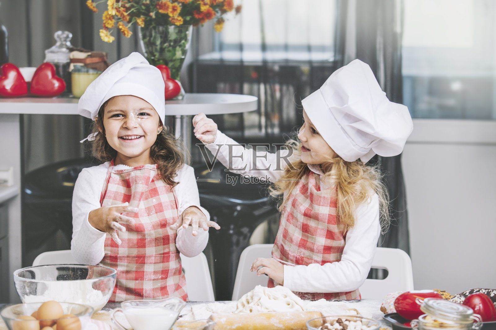 两个快乐的小女孩在厨房的桌子上用面粉和面团做饭是可爱和美丽的照片摄影图片