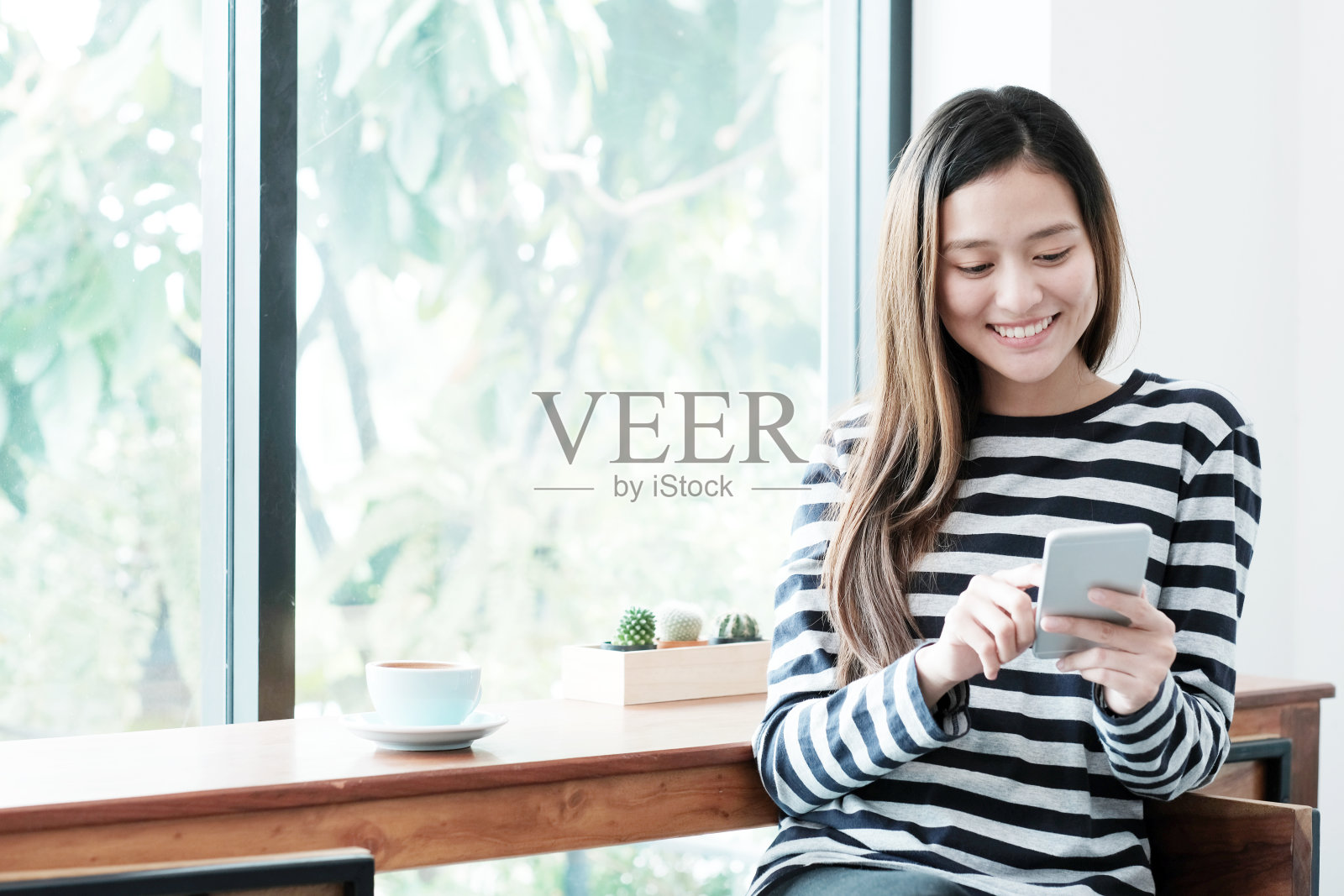 年轻的亚洲女子使用智能手机，而坐在窗口咖啡馆背景，人的技术和生活方式照片摄影图片