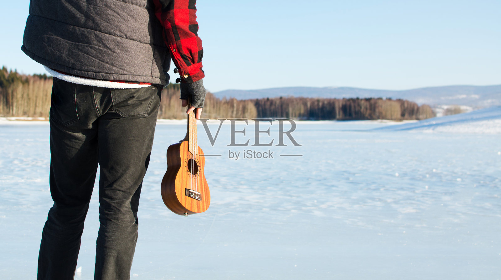 在结冰的湖面上，拿着尤克里里琴的男人照片摄影图片