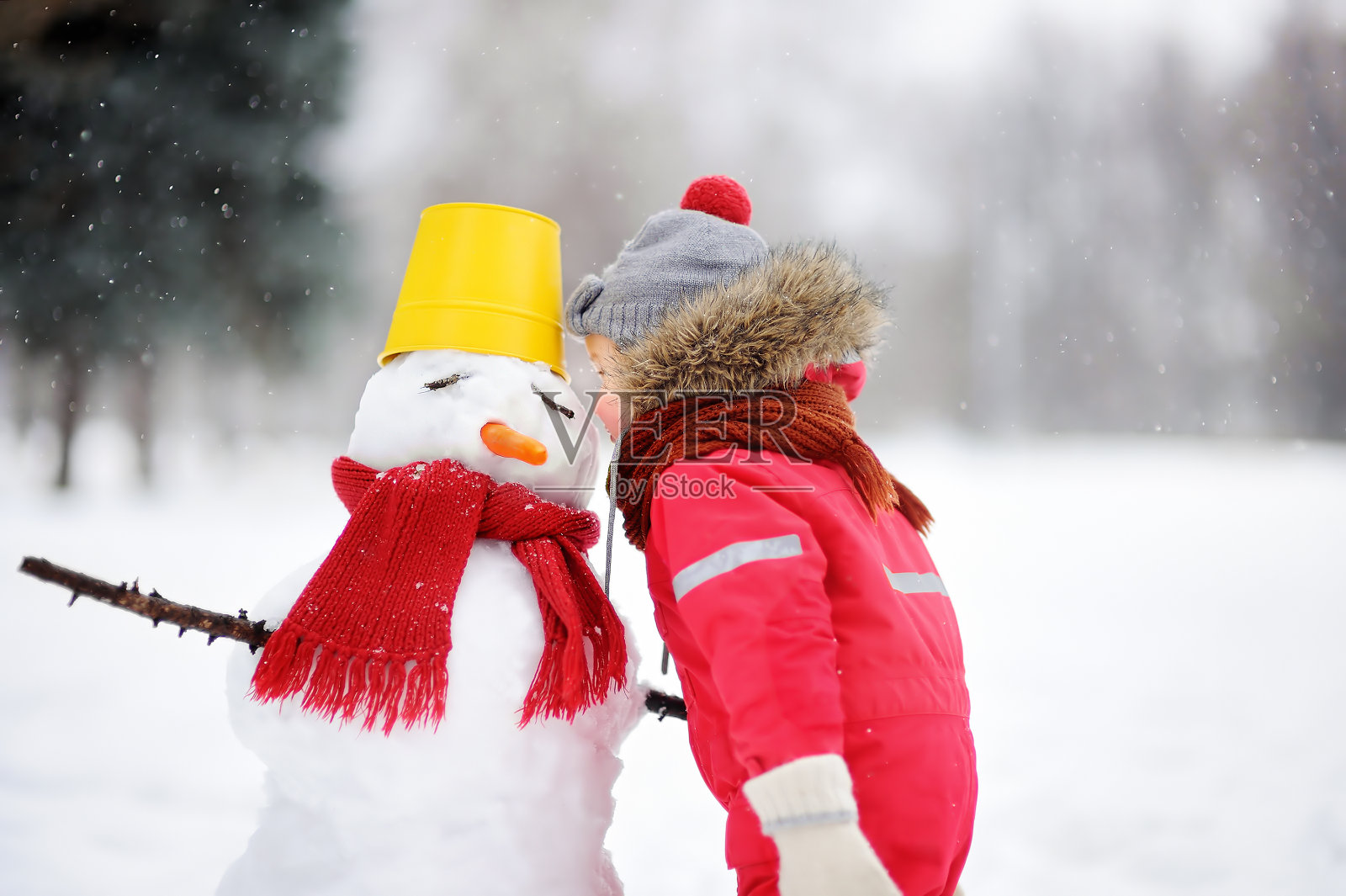 穿着红色冬衣的小男孩在雪天公园里玩雪人照片摄影图片