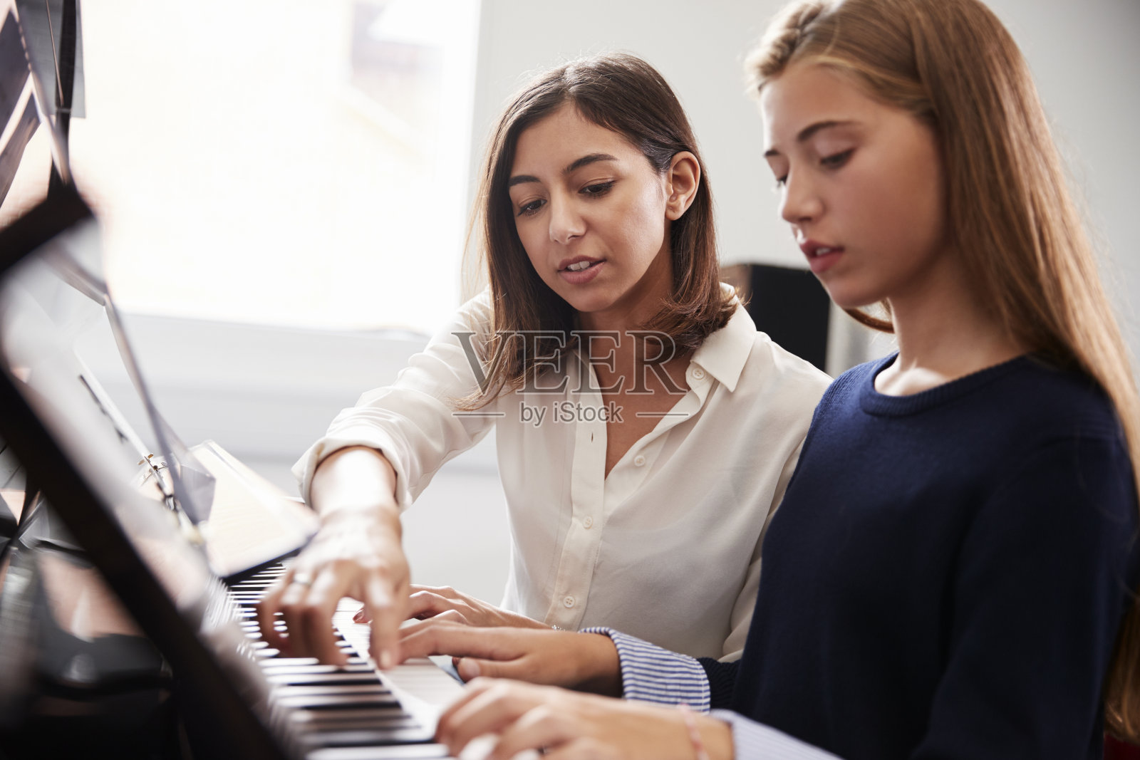 在音乐课上，女学生与老师一起弹钢琴照片摄影图片