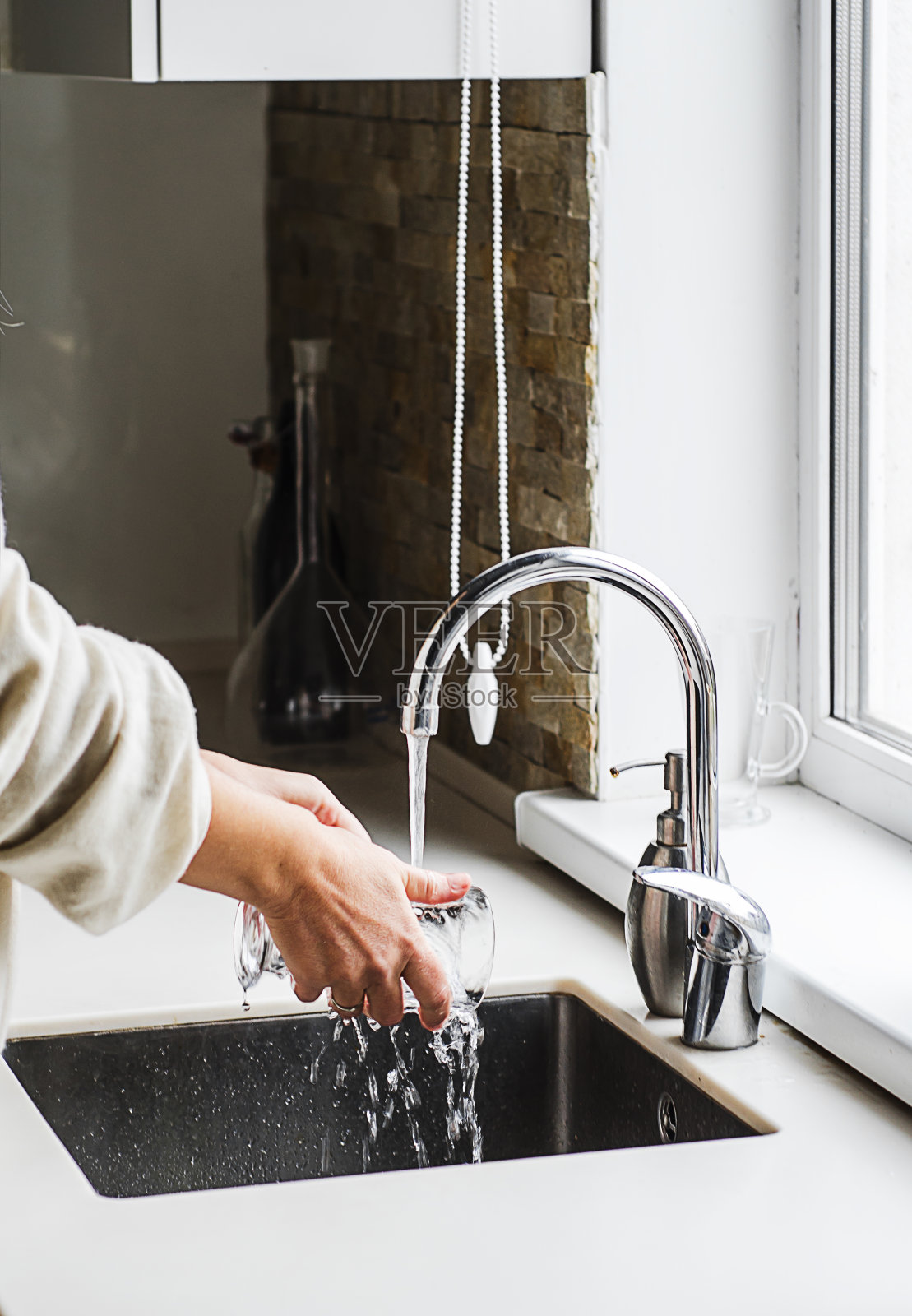 女人用手洗盘子或在厨房的水龙头上倒新鲜的饮用水照片摄影图片