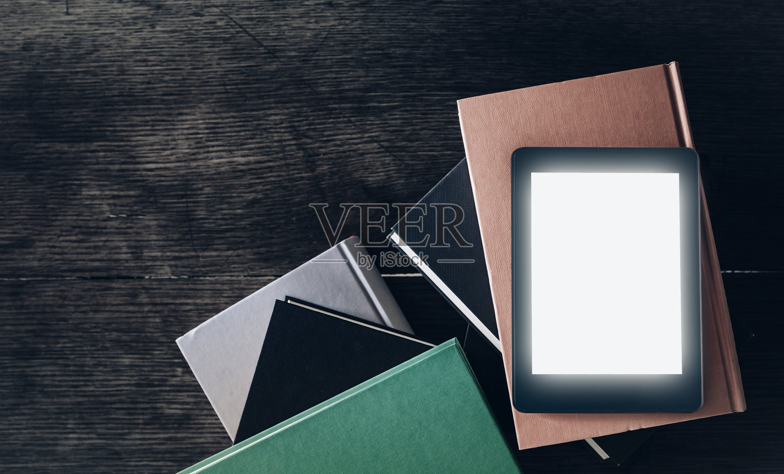在质朴的木桌上的一堆书上放着发光的电子阅读器照片摄影图片